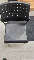 Front view of black and silver stacking chair showing perforated backrest and contoured seat.