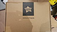 Closed brown cardboard box with Tommee Tippee logo and slogan 'helping you Parent On' imprinted.