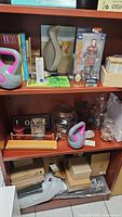 Photo showing various items on shelves including kettlebells, boxes, figurines, jars, and lampshade on top of a wooden cabinet.