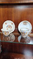 Two teacups with their matching saucers displaying portraits of King George VI and Queen Elizabeth II coronations, floral and emblematic details, gold rim accents.