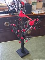 Photo showing the lighted decorative tree with red cardinal birds perched on black branches with red berries, standing on a black square base.