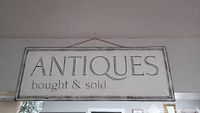 Photo of rectangular metal sign with 'ANTIQUES bought & sold' text, showing its painted surface and hanging cord.