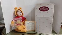 Ashton Drake Winnie the Pooh doll with a small sealed Pooh plush, certificate of authenticity, and original box against white backdrop.