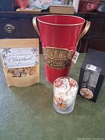 Full lot view showing red Christmas bucket, gingerbread simmer mix, Cinnabon candle, and its packaging box on a flat surface.