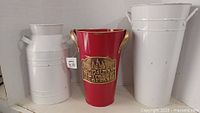 Photo of three decorative metal containers: two white milk jug style containers and one red bucket with gold handles and Christmas Tree Farms plaque.