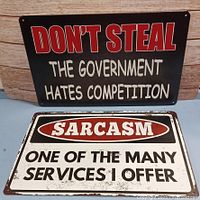 Photo shows two humorous metal signs, one black and one white, both measuring 8" x 12".