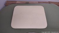 Top side of Pampered Chef baking stone, light beige rectangular stoneware with rounded corners, showing smooth surface with some light marks.