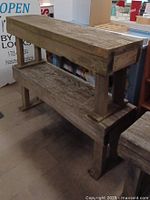Photo showing a rustic barn wood bench with a lower shelf. The bench is heavy and rough textured, constructed from aged wood planks with weathered patina.