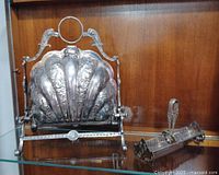 Biscuit warmer with ornate shell-shaped lid on stand; sugar cube holder and tongs to the right on shelf