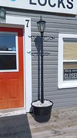 Full view of black metal solar lamp post with lantern-style top in a large black planter filled with white stones, placed outside building next to red door.
