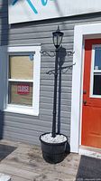 Full view of black solar lamp post standing in black planter with white stones next to a grey building and orange door.