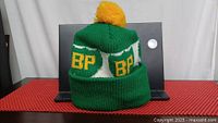 Front view of green and yellow knitted BP branded toque with pompom on top. Shows fold-up cuff with BP logos surrounding the band.