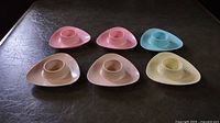 Set of six vintage Melmac melamine egg cups arranged on a dark surface, showing the top view with triangular bases and central egg holders visible.