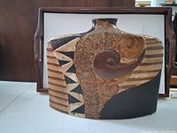 Front and side angle of the flat vintage ceramic vase showing geometric and swirl motifs in brown and black.