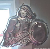 Close-up photo of the Wilton He-Man cake pan, showing He-Man holding sword and shield
