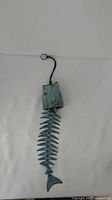 Full view of the turquoise fish wind chime showing the fish head with hanging loop and the spine with fins and tail segments connected by metal loops.