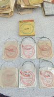 Photo showing eight packs of Guild guitar strings, some sealed and some worn, with coiled metallic strings visible.