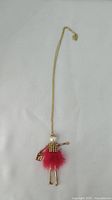 Full view of gold-tone necklace with pendant shaped like a girl wearing a jeweled top and red fluffy skirt.
