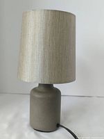 Front view of small grey ceramic base table lamp with beige fabric shade.
