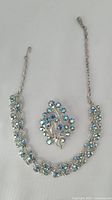 Vintage Coro necklace and brooch on white background, showing silver-tone metal with blue rhinestones arranged in floral patterns. Necklace chain extended with clasp visible.