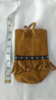 Front view of vintage brown suede leather drawstring bag with embroidered trim and fringe showing approximate length with measuring tape
