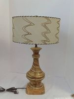 Full view of vintage mid-century modern table lamp with beige fiberglass drum shade featuring wavy brown line patterns and ceramic base with brown swirls and gold highlights.