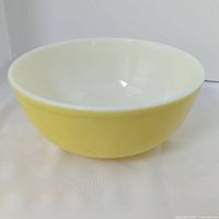 Side angle view of the yellow vintage Pyrex mixing bowl showing yellow exterior and cream-white interior.