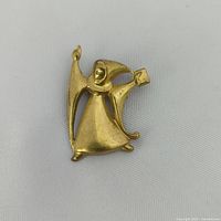 Close-up photo of gold-tone wizard brooch showing detail of figure, hat, book and raised arm casting spell.