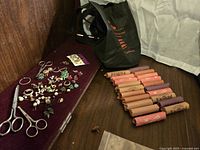 Overview of the lot showing various earrings spread on a surface with two pairs of metal scissors and multiple rolls of pennies with a black tote bag in the background.