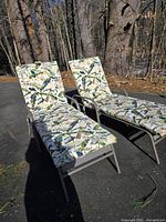 Two outdoor lounge chairs positioned side by side outside, showing cushions with tropical leaf pattern.