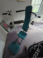 AB Cruncher exercise machine showing padded backrest, arm rests, foot support and part of its white frame in room with carpet and window light.