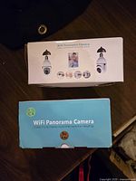 Two boxed WiFi Panorama cameras on a dark surface, showing front product packaging details.