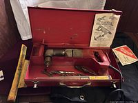 Open metal Milwaukee branded case showing the right angle drill, drill bits, and attachments laid out inside with yellow Irwin packaging.