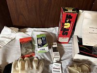 Photo of lot showing several items including gloves, electrical gadgets in packaging, white cloth, candles in glass holders.