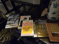 Seven novels visible on a wooden surface including Into Thin Air, The Road Less Traveled, Maplethorpe, and others.