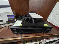 Onkyo receiver placed on wooden surface with cables and manual on top, front panel view.