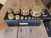 Photo showing 13 brass calibration weights arranged on case with serial number 1036 visible.