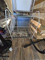 White metal wire two-tier shoe rack with wire shelving, viewed front and top angles in light indoor space with wood flooring.