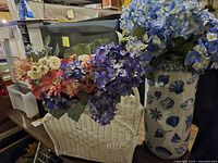 Photo showing white woven basket filled with various artificial flowers in shades of pink, cream, coral, and purple