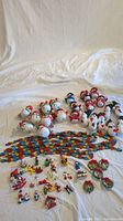 Wide photo showing a collection of snowman ornaments, miniature wooden and resin Christmas decorations laid out on a white surface.