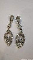 Pair of silver-tone rhinestone dangle earrings laid flat on white background showing front view with marquise-shaped dangling part.