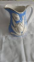 Front and side view of the ceramic pitcher showing silver floral designs and blue background