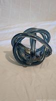 Blue glass knot sculpture shown from one angle on white background.