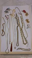 Overview of mixed costume jewelry spread on white background showing various chains, pendants, brooches and earrings in gold and silver tones.