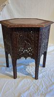 Full view of hexagonal side table showing carved peacock design and legs.