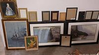 Photo showing a collection of framed and empty picture frames against a white wall, including Niagara Falls prints and paintings.