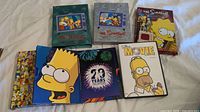 Seven DVD cases of The Simpsons laid out on a white surface showing different characters and themes representing different seasons and a movie.