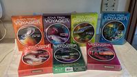 Photo showing all seven DVD box sets for Star Trek Voyager seasons 1 to 7 arranged in two rows on a flat surface.