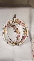 Teacup and saucer set with floral pattern on white porcelain, including a gold-rimmed handle and stand