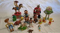 Photo showing vintage and mixed character toys including Woody on Bullseye, Mr. and Mrs. Potato Head, Buzz Lightyear, Simpsons characters, and other small figures against a white background.